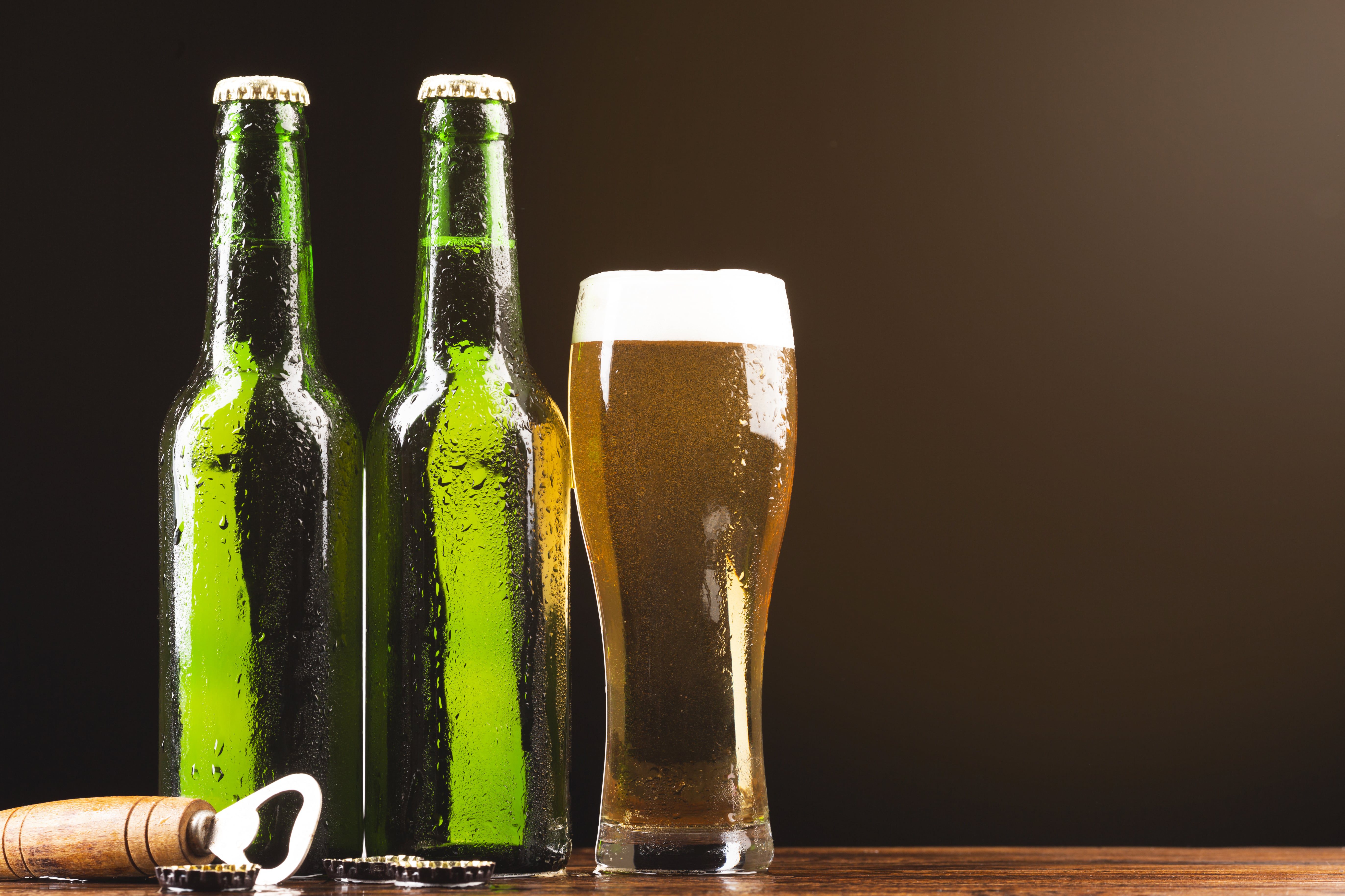 Duas garrafas de vidro de cerveja com um copo cheio de cerveja ao lado e um abridor de cerveja.